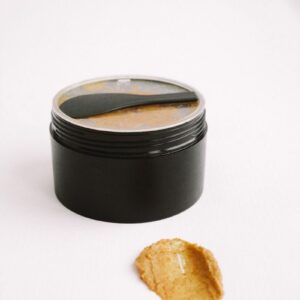 Black cosmetic jar and spread honey scrub against a clean white backdrop.