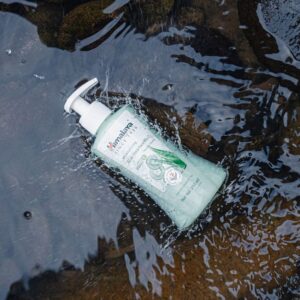 Bottle of Himalaya face wash floating in a clear stream with natural rock background.