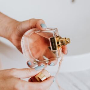 Close-up of a woman's hands holding an elegant perfume bottle inside a brightly lit room.
