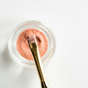 brown makeup brush in front pink powder on glass case