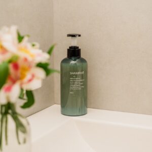 a bottle of shampoo sitting on a sink next to a vase with flowers